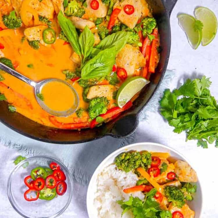 overhead photo of a cast iron skillet with red curry, chicken, asil, and sliced peppers, with a bowl of rice and red curry next to it