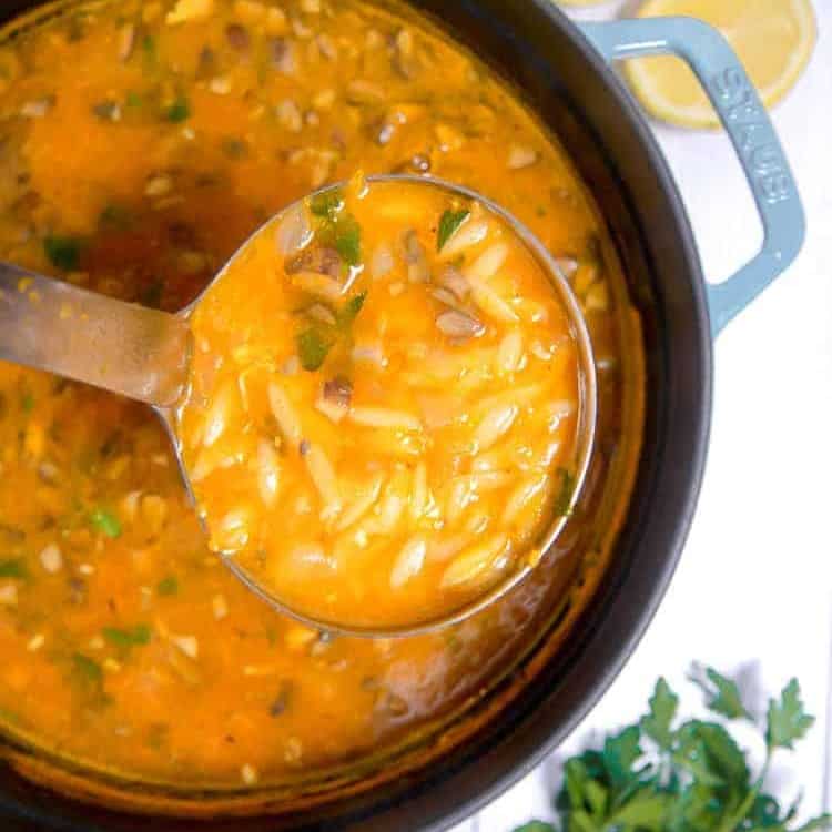 dutch oven pot with vegetable orzo soup being lifted out with a ladle spoon