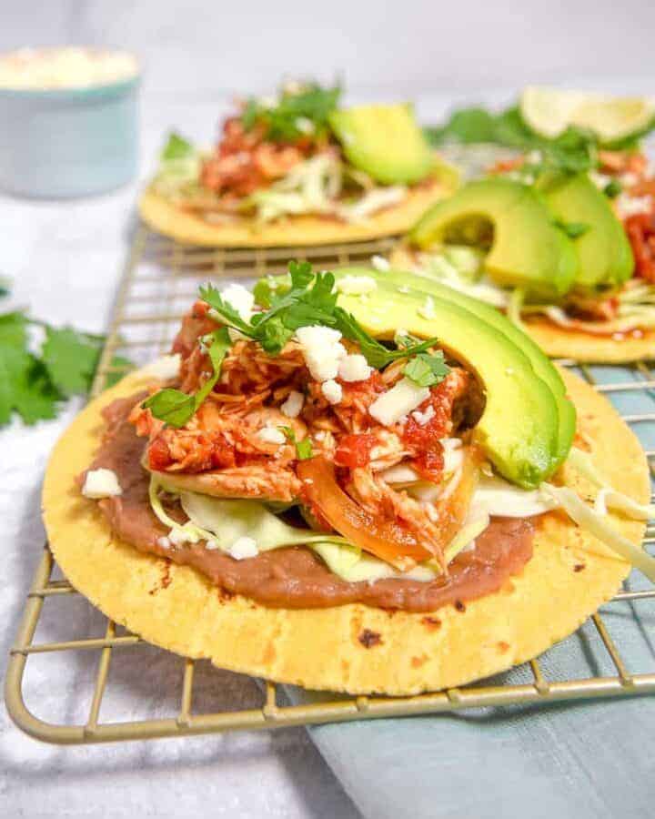 close up of shredded chicken tinga on corn tortillas with refried beans, lettuce, and avocado