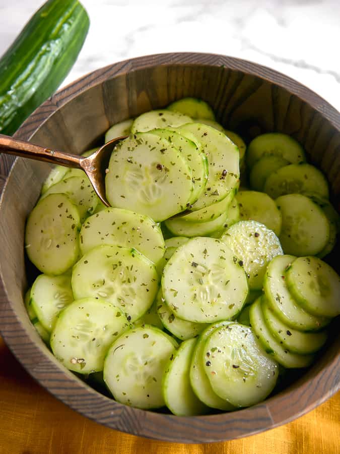 Close up of spoon lifting cucumbers out of a wooden bowl