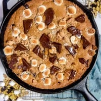 overhead photo of large s'mores cookie in a cast iron skillet with melted chocolate, toasted marshmallows, and graham crackers on top