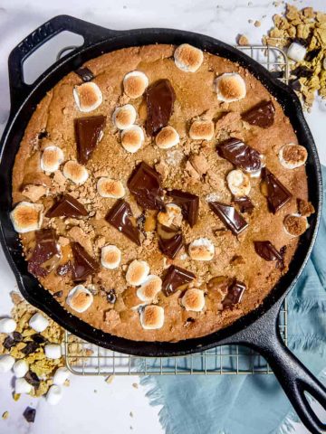 overhead photo of large s'mores cookie in a cast iron skillet with melted chocolate, toasted marshmallows, and graham crackers on top
