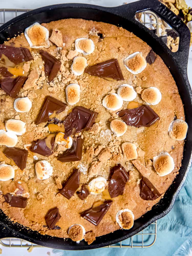 close up of overhead photo of large s'mores cookie in a cast iron skillet with melted chocolate, toasted marshmallows, and graham crackers on top