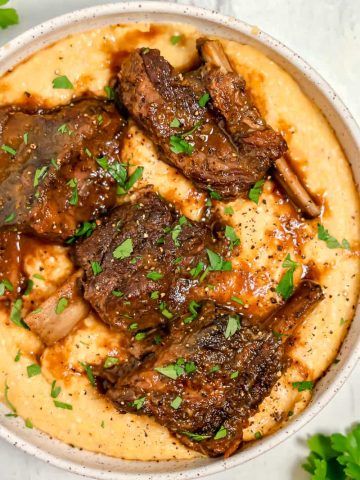bowl of polenta with 4 beef short ribs and gravy on top