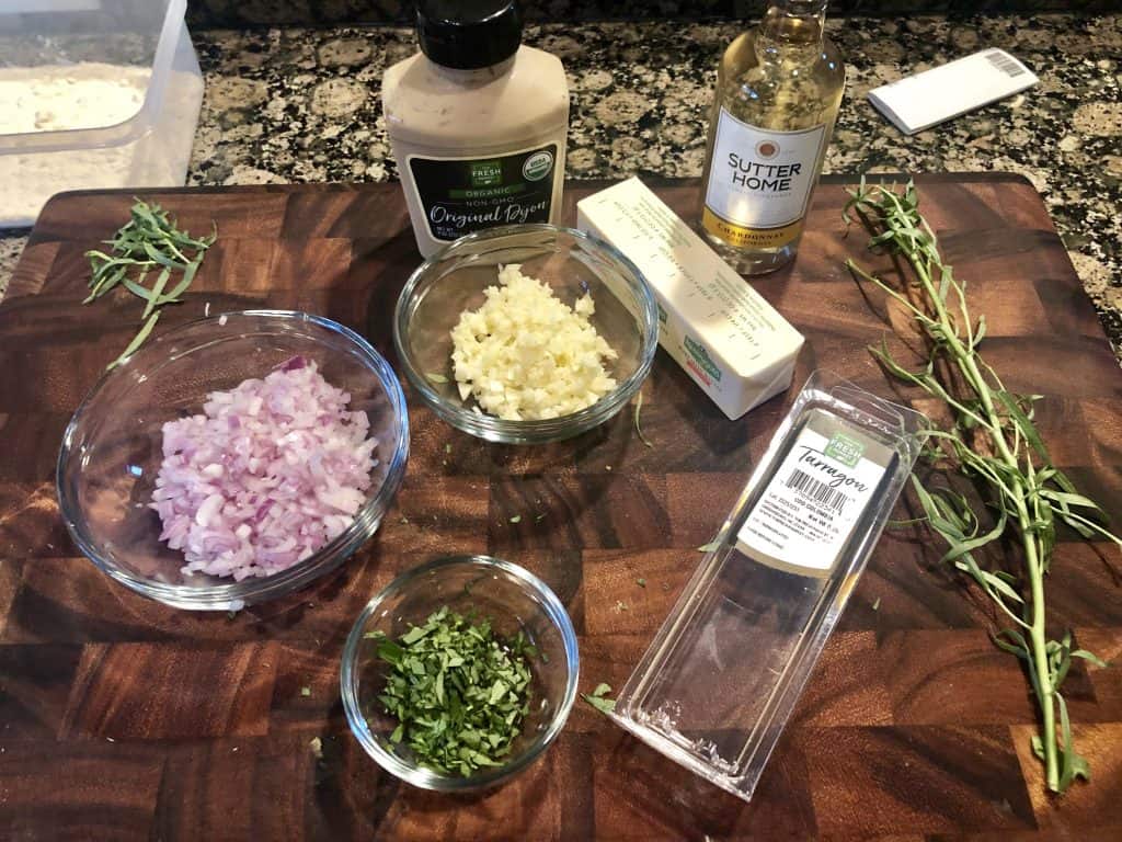 photo of a cutting board with minced shallot, minced garlic, fresh taragon in a bowl, dijon mustard, and a fresh tarragon plant