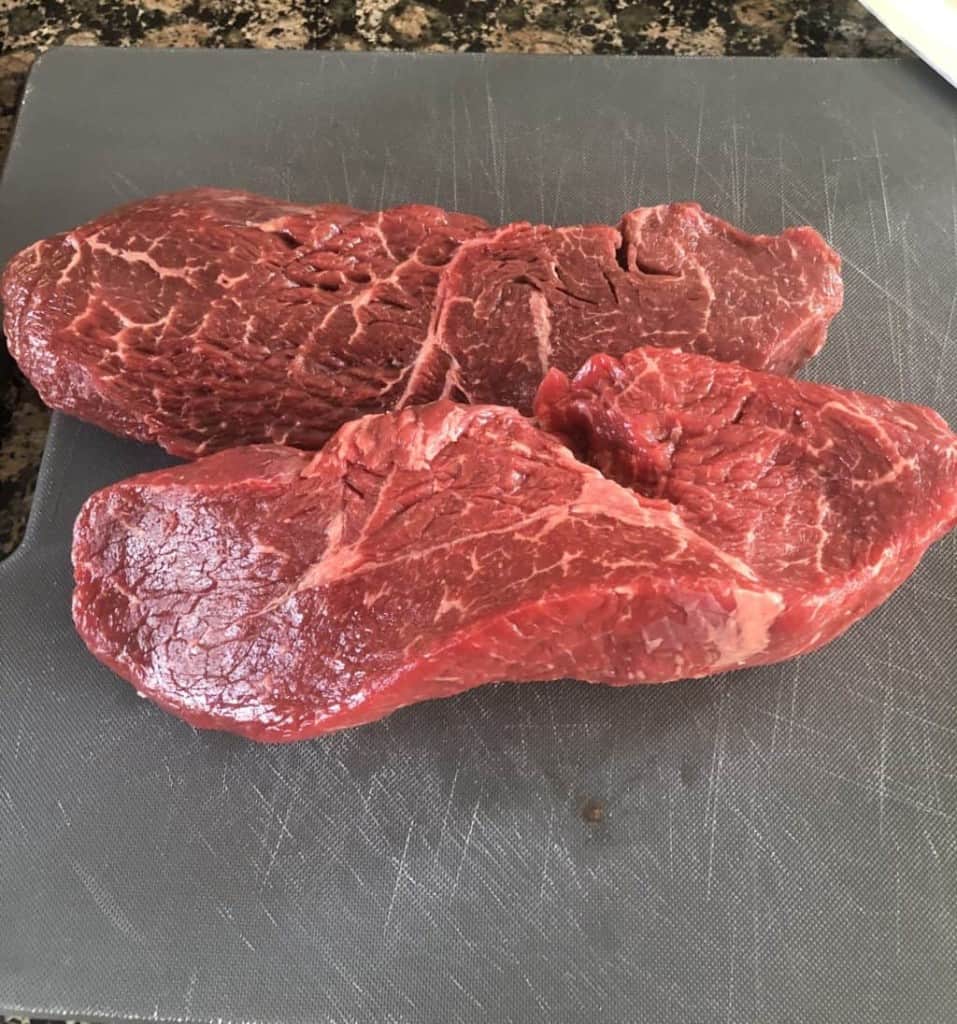 two uncooked sirloin steaks on a cutting board