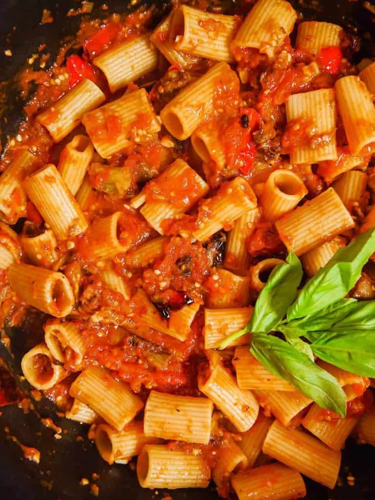 roasted eggplant, bell peppers, rigatoni pasta, and red sauce in a dutch oven with fresh basil leaves