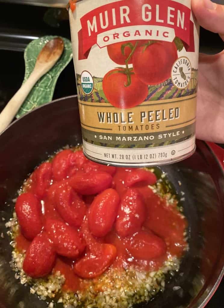 a can of whole peeled tomatoes being held over pot with tomatoes inside
