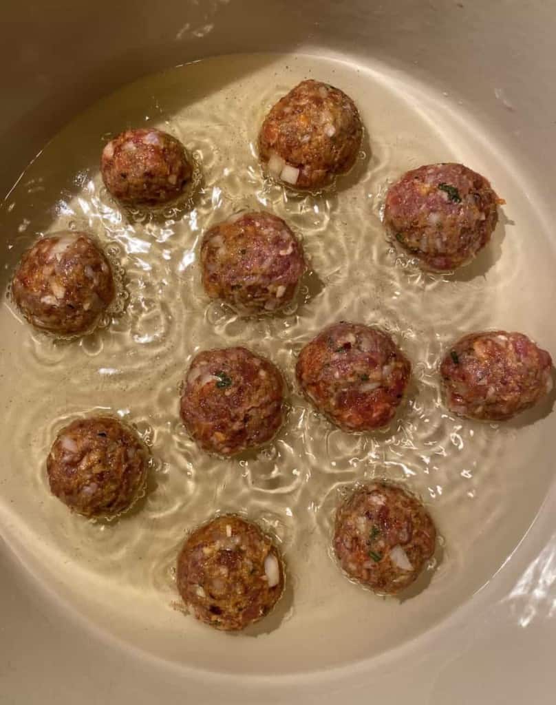 meatballs searing in a dutch oven in oil