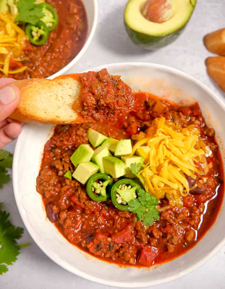 bowl of chili with a scoop being taken out with toasted bread