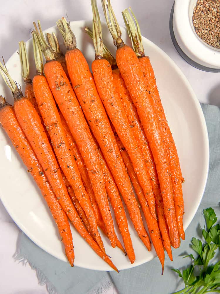 overhead of roasted carrots on a white plate with coriander seeds