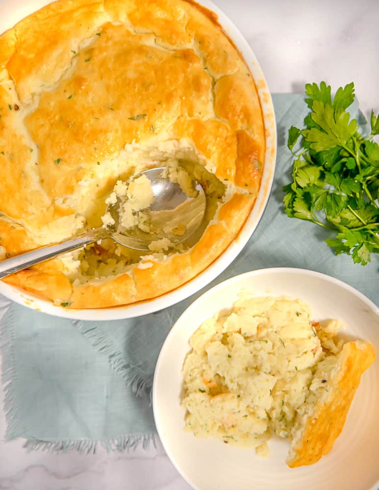 overhead photo of potato soufflé in a large ramekin with a big spoon removed and placed in a white bowl to the side