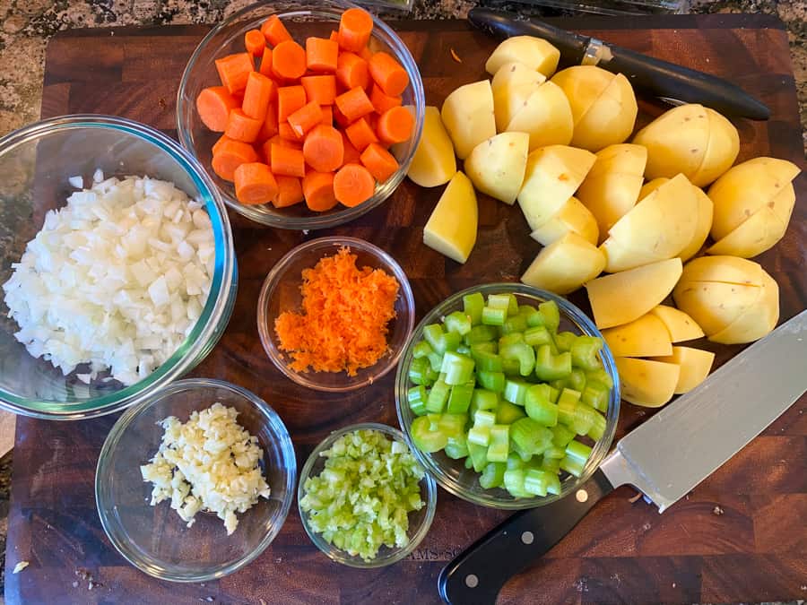 chopped carrots, celery, onion, garlic, and potatoes in bowls on a cutting board