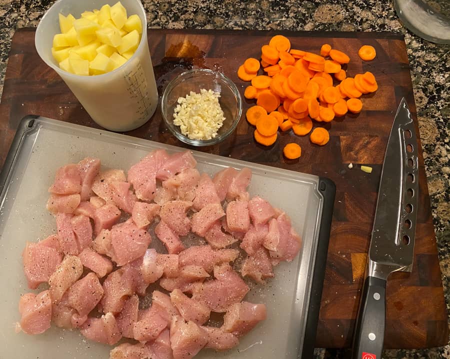 cut up chicken on a cutting board, sliced carrots, diced potatoes, and minced garlic