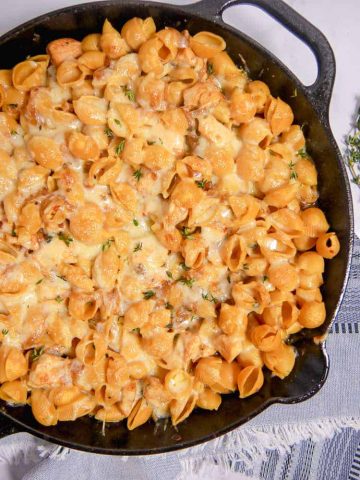 a cast iron skillet with pasta shells and melty cheese inside with a blue napkin underneath
