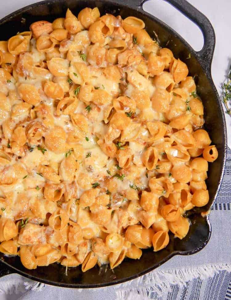 a cast iron skillet with pasta shells and melty cheese inside with a blue napkin underneath