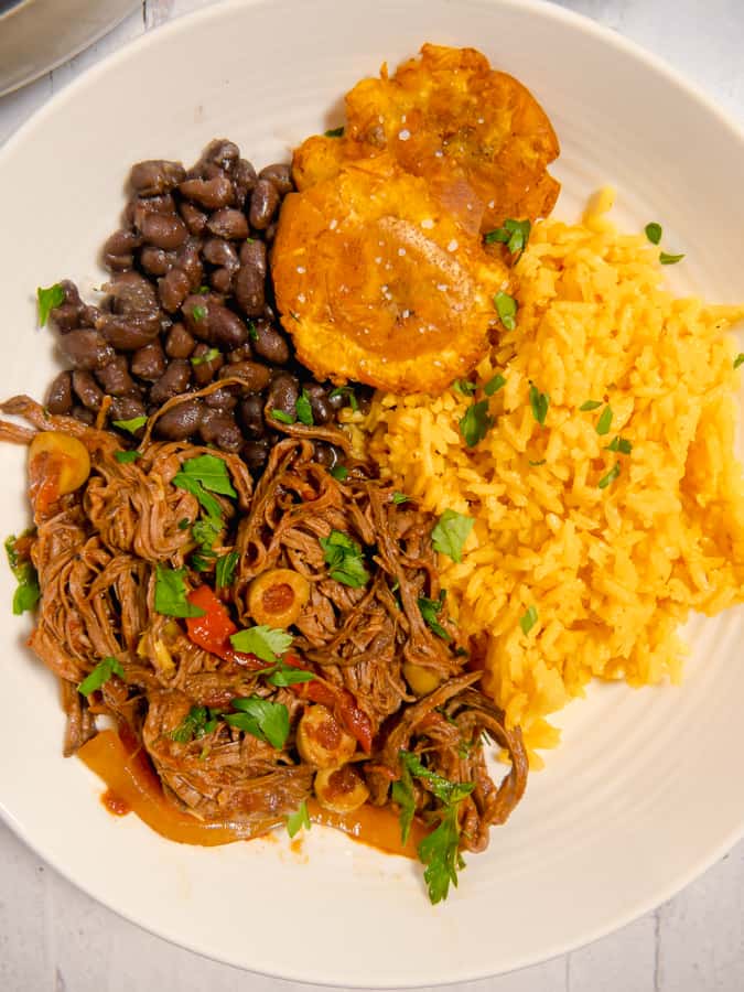 plate of ropa vieja, yellow rice, black beans, and crispy tostones