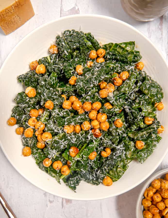 overhead photo of kale caesar salad topped with chickpeas and parm cheese with bowl of chickpeas to the side