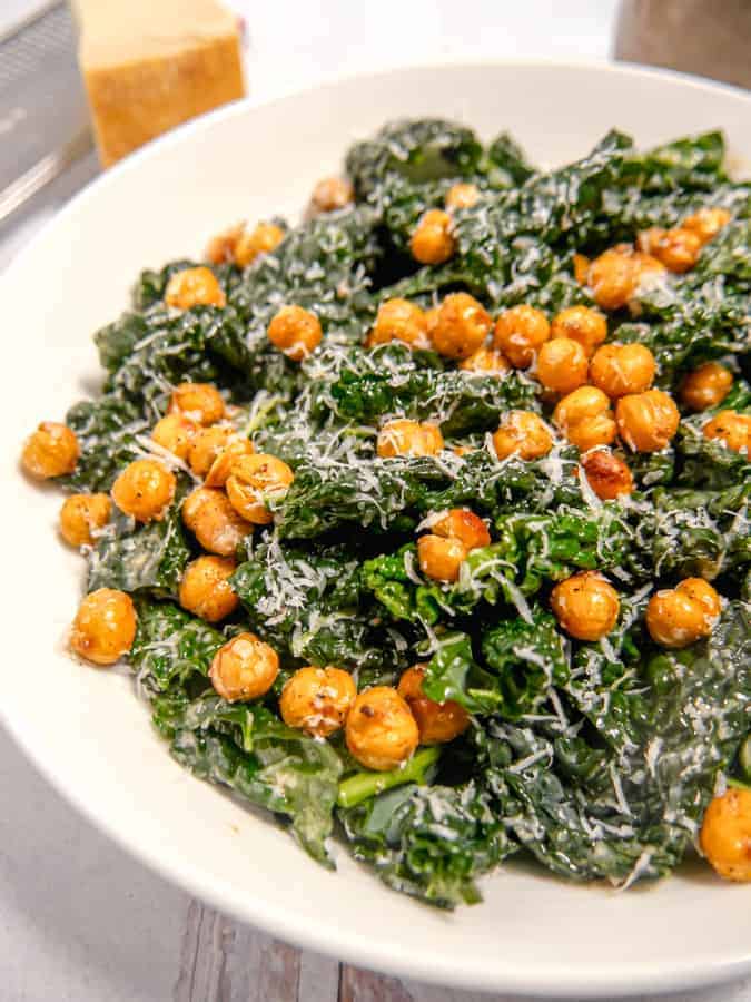 zoomed in photo of kale caesar salad in a bowl topped with parmesan and chickpeas