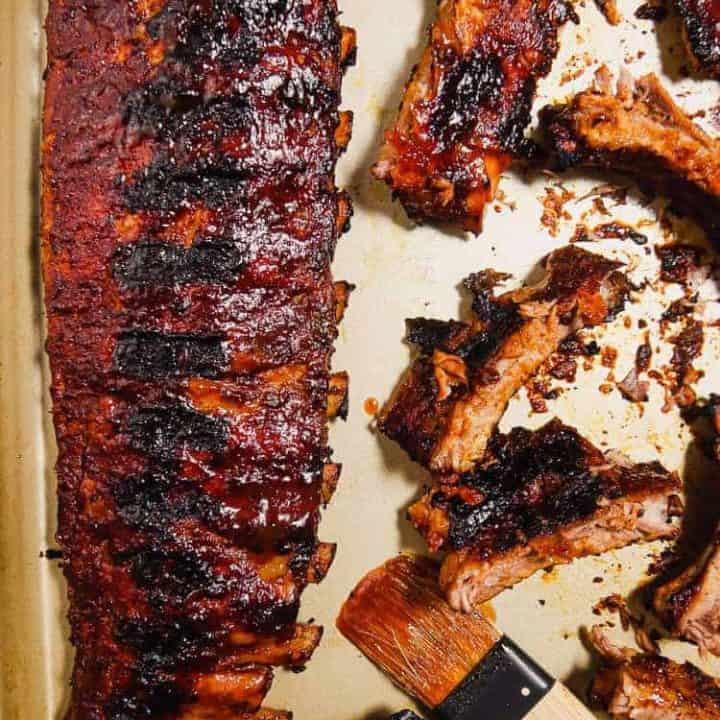 overhead shot of rack of bbq grilled ribbs and cut ribs on a platter with bbq brush