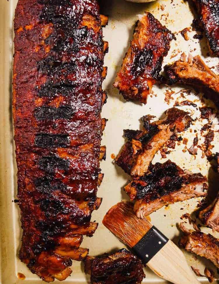 overhead shot of rack of bbq grilled ribbs and cut ribs on a platter with bbq brush