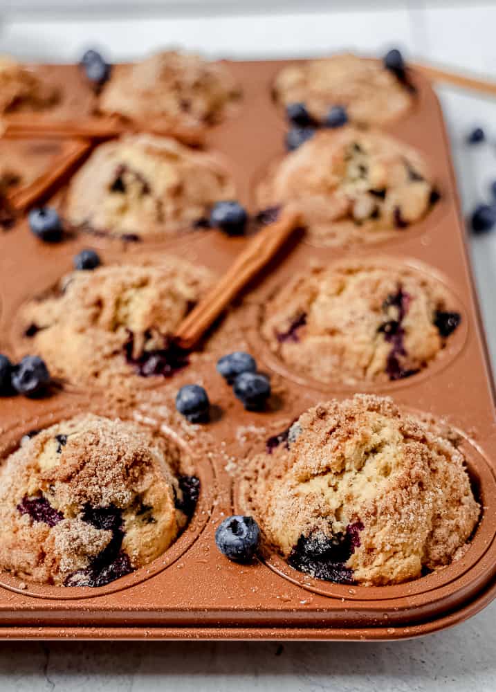 close up of copper muffin tin with blueberry muffins and loose fresh blueberries around