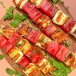 overhead photo of grilled watermelon and halloumi cheese on skewers topped with fresh herbs