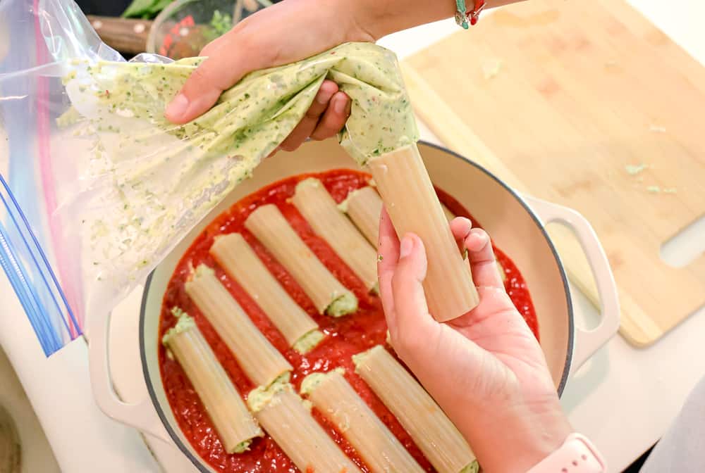 photo showing pesto filling being pipped into the cooked manicotti 