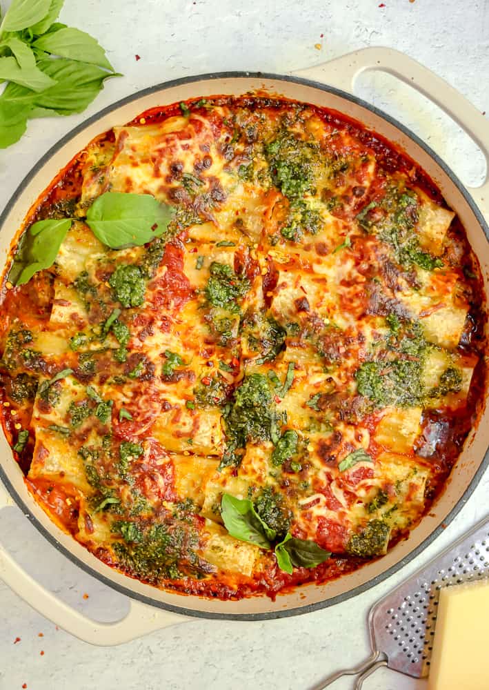 overhead photo of white casserole dish with cheesy pesto filled manicotti, in a bed of red sauce, and topped with browned bubbly cheese