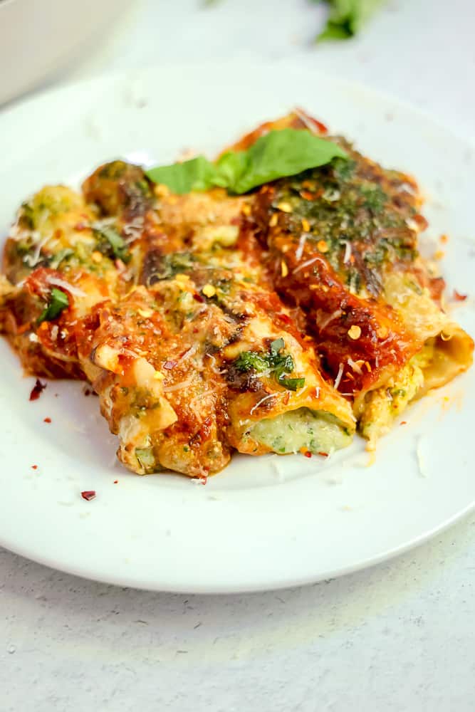 close up of three manicotti's on a white plate with pesto and red sauce