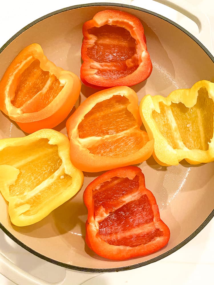 red, orange, and yellow bell peppers halved and in a casserole dish