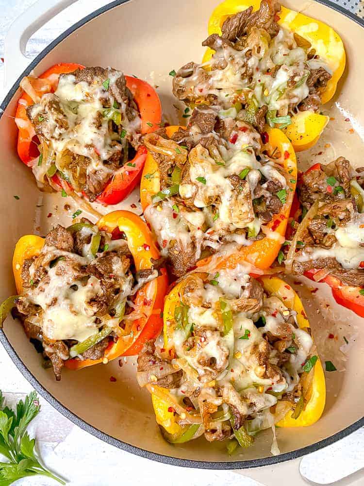 a white casserole dish with colored bell peppers stuffed with steak, cheese, onions, and peppers on a white backdrop