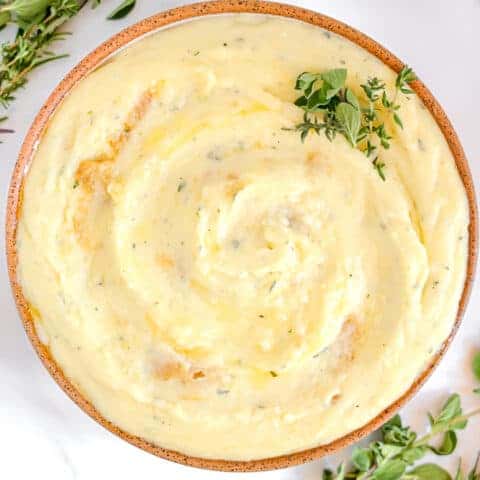 garlic and herb mashed potatoes in a bowl surrounded by fresh herbs