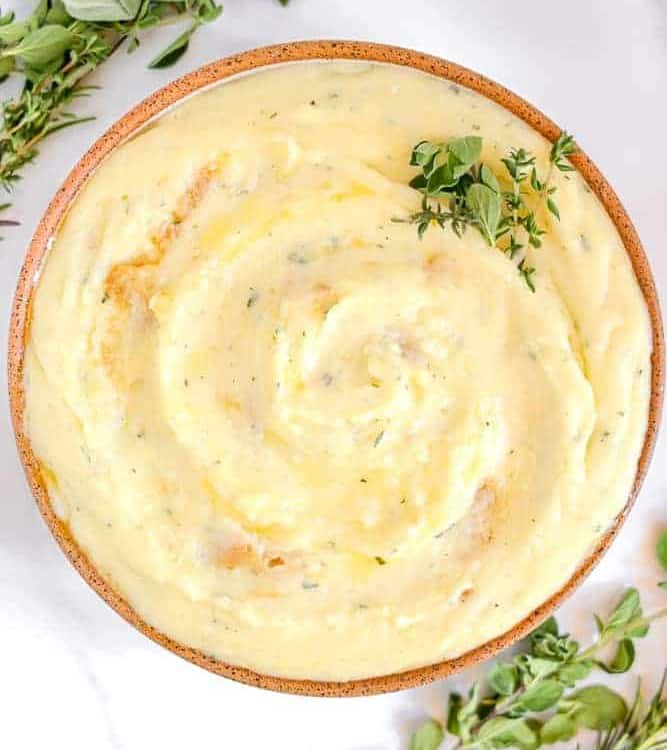 garlic and herb mashed potatoes in a bowl surrounded by fresh herbs