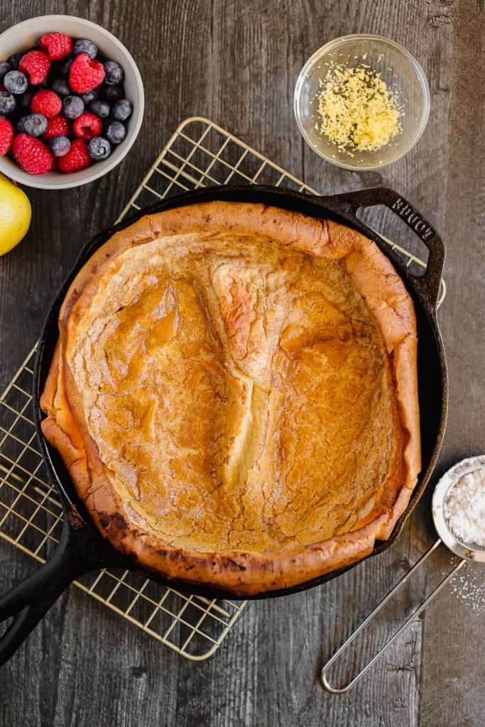 dutch baby pancake in a cast iron with a bowl of berries