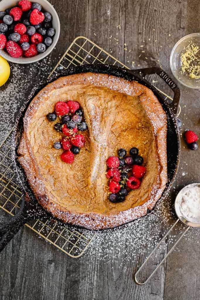 dutch baby pancake in a cast iron topped with sugar, berries, and lemon
