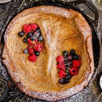 cast iron skillet with a dutch baby pancake, berries, and powdered sugar sprinkled over the top