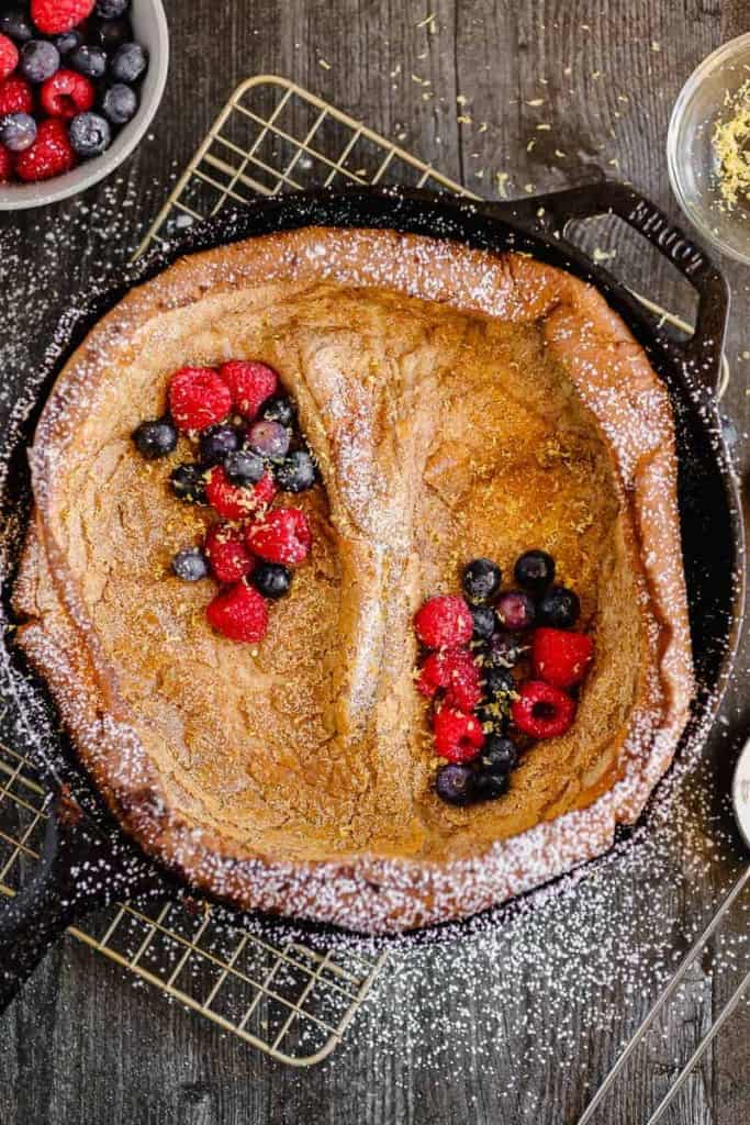 cast iron skillet with a dutch baby pancake, berries, and powdered sugar sprinkled over the top