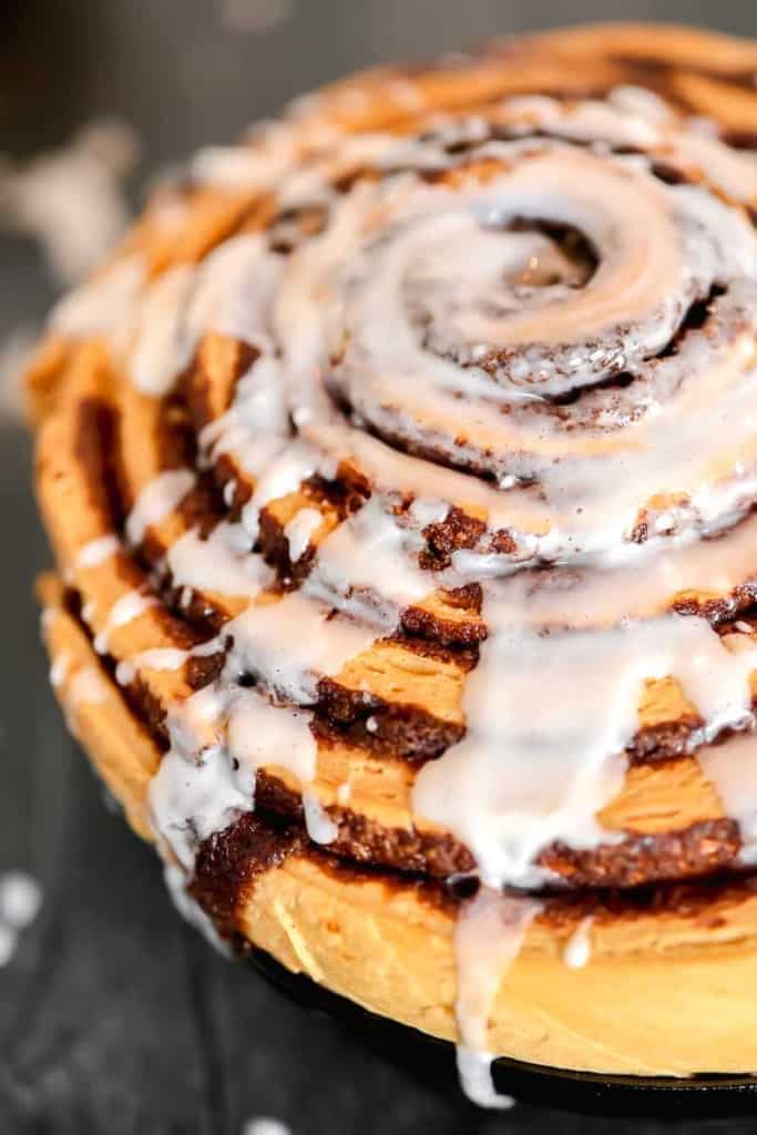 close up of cinnamon roll with icing drizzled on top