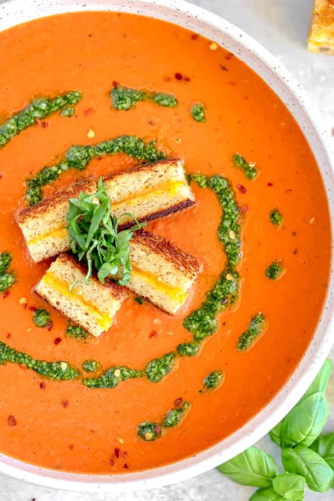 bowl of roasted red pepper tomato soup with grilled cheese croutons and basil swirl