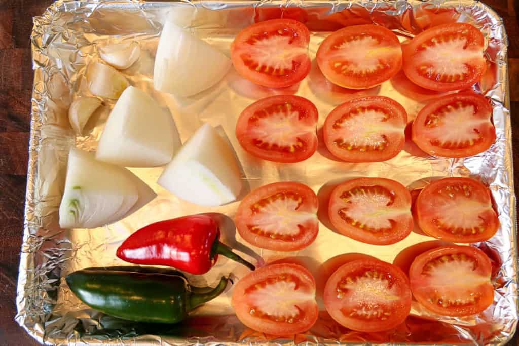 halved roma tomatoes, quartered onions, and hot peppers on a sheet pan