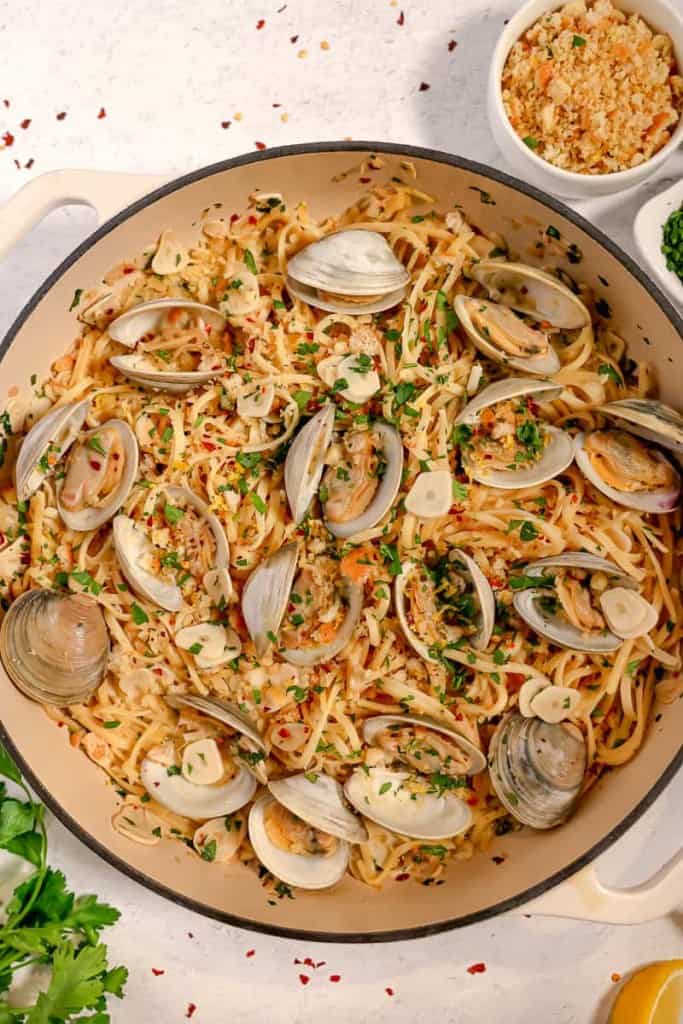 linguine and clams in a white wine sauce with breadcrumbs and fresh herbs in the background