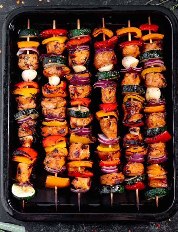 grilled chicken skewers and vegetables on a black dish