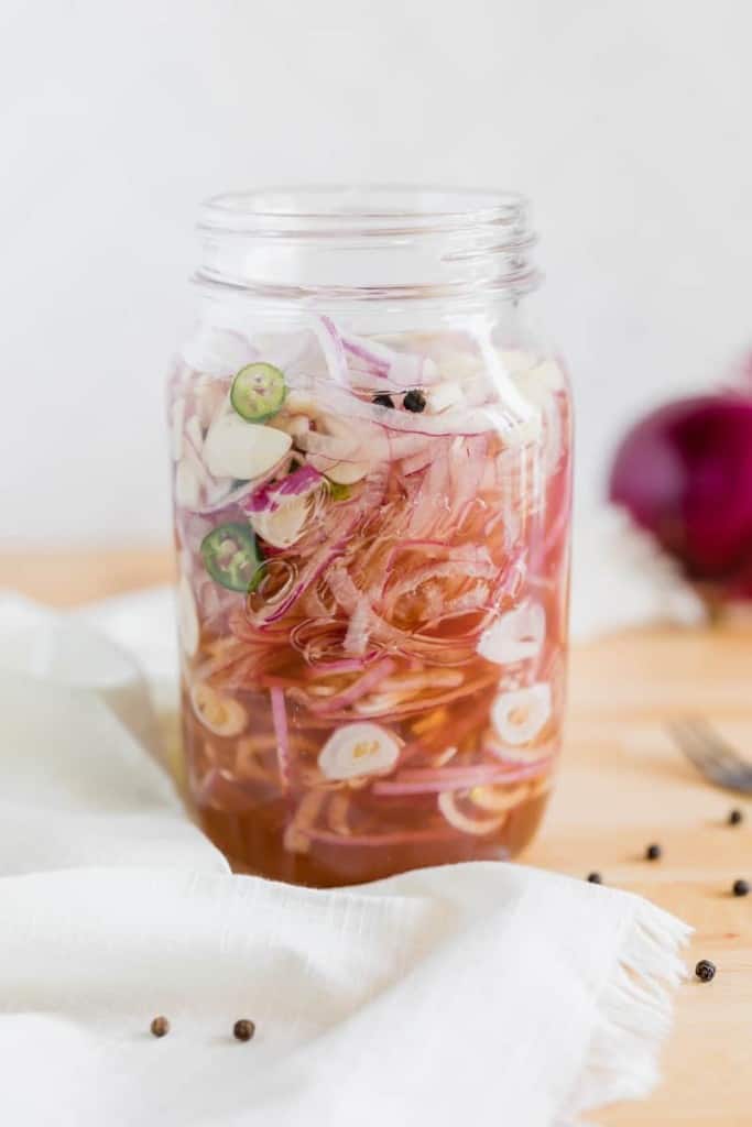 sliced red onions in a glass jar with brine poured inside.
