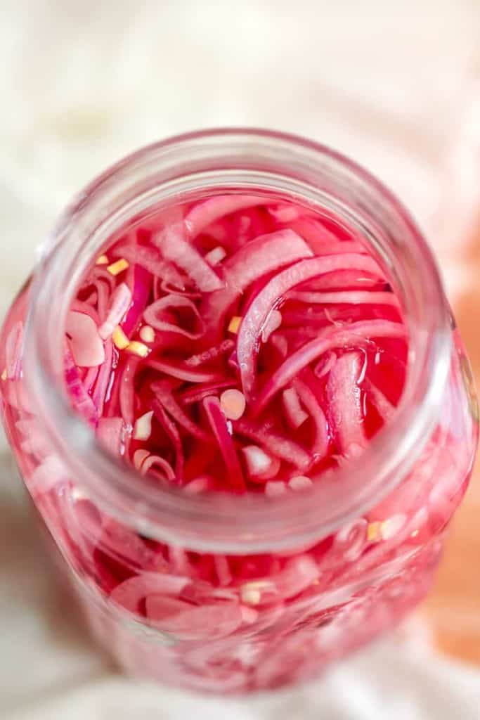 overhead shot of open clear jar with pickled red onion inside 