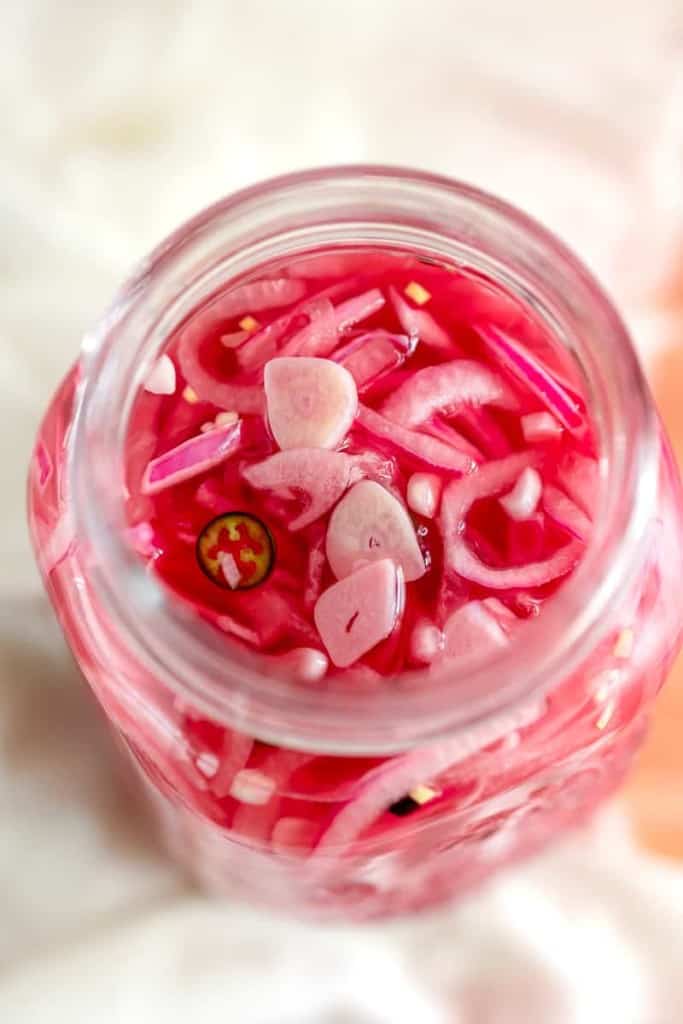 overhead photo of clear jar with pickled red onions and sliced garlic
