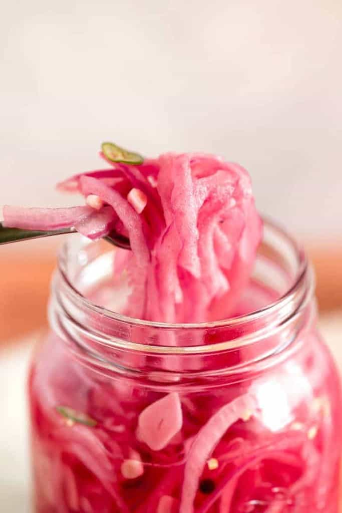 glass jar with a fork lifting pickled red onions out of the jar