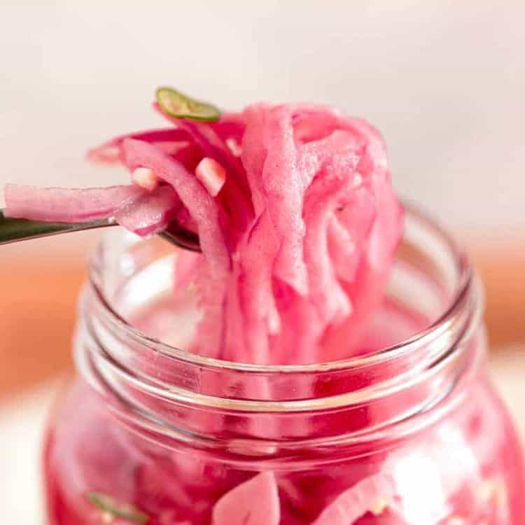 glass jar with a fork lifting pickled red onions out of the jar