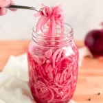 Jar full of pickled red onions with a fork lifting onions out of the top