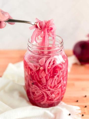 Jar full of pickled red onions with a fork lifting onions out of the top